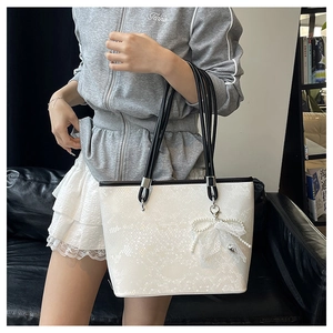 Detail of white snakeskin tote bag featuring a pearl and lace bow charm decoration