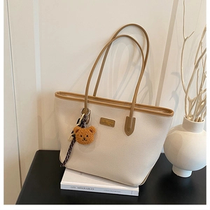 Dettaglio della borsa tote beige con texture in pelle litchi e ciondolo a orsetto