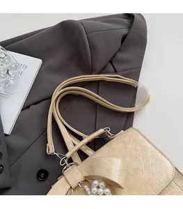 Detail of beige bow crossbody bag with pearl charms on a gray blazer background