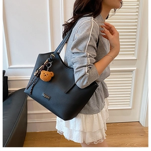Detail of black pebbled leather tote bag with metallic logo and brown bear charm accessory