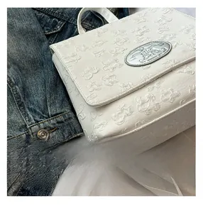 Detailansicht eines weißen Rucksacks mit geprägtem Schmetterlingsmuster und Metallplakette