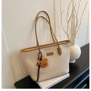 Dettaglio borsa tote beige con finiture in pelle marrone e ciondolo a orsetto