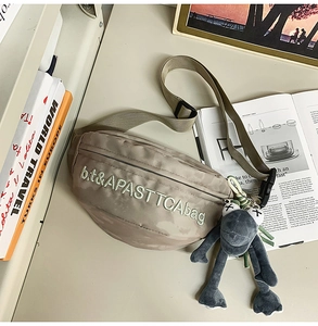 Detail of khaki canvas chest bag with white embroidery and gray frog plush keychain accessory