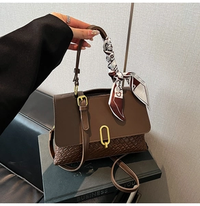 Close-up of brown woven handbag with gold clasp, silk scarf handle, and adjustable strap