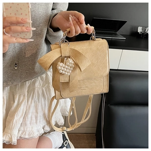 Close-up of cream textured leather handbag with bow detail and pearl heart pendant