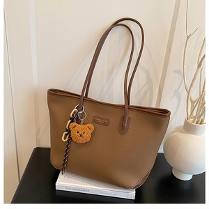 Dettaglio della borsa tote in pelle marrone con ciondolo orsetto e logo del marchio