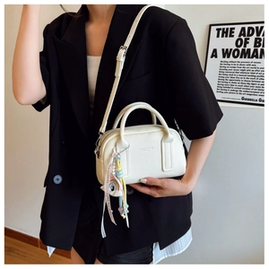 Detail of white pebble leather handbag with rainbow tassel and decorative ribbon charm