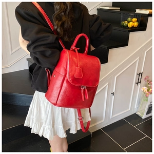 Detail shot of a bright red faux leather backpack featuring a top handle and metal zippers