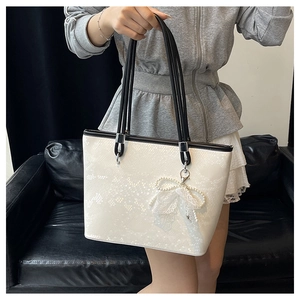 Detail of off-white tote bag with snake skin texture and pearl bow pendant decoration