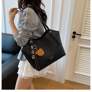 Detail of black pebbled leather tote bag with gold logo and brown teddy bear charm