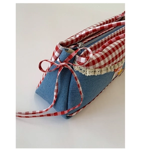 Close-up of denim shoulder bag with red checkered trim and delicate lace detail