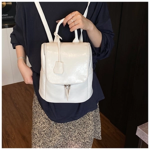 Detail of a minimalist white faux leather backpack featuring a top handle and side zippers