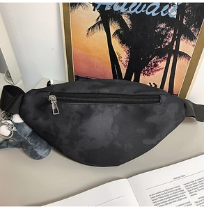 Close-up of black tie-dye chest bag with silver zipper and a cute plush doll keychain