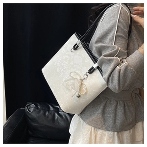 Detail of white lace embossed tote bag featuring pearl bow charm and black leather handle