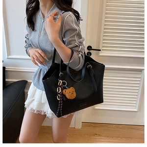 Close-up of black leather tote bag with metal logo and cute brown teddy bear keychain accessory