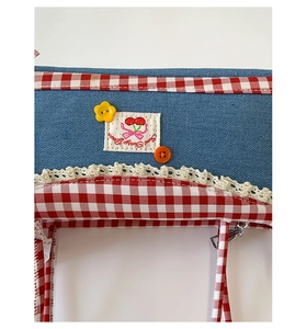 Close-up of retro denim bag with red check trim, white lace, and cherry embroidery