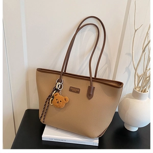 Dettaglio di una borsa tote beige con grana litchi e un ciondolo a forma di orsetto