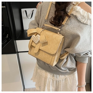 Detail of cream bow backpack showing textured leather and pearl heart charm on model