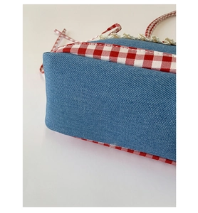 Close-up of blue denim handbag featuring red plaid trim and white lace embroidery