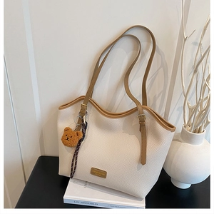 Detail of lychee textured leather tote with contrast brown trim and teddy bear charm