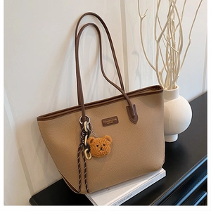 Dettaglio della borsa tote in pelle kaki con ciondolo a forma di orsetto e logo in metallo