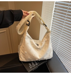Close-up of cream canvas tote bag featuring textured fringe details and black shoulder strap
