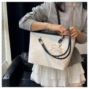 Detail of white snakeskin tote bag featuring lace bow and pearl charm accessories
