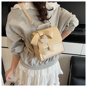Close-up of cream beige ribbon backpack with a pearl heart pendant and glossy leather texture