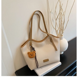 Close-up of cream pebble leather tote bag featuring a brown plush bear charm and long straps