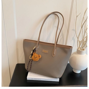 Dettaglio della borsa tote taupe con texture motivo litchi e ciondolo a forma di orsetto