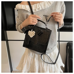 Detail of a black glossy shoulder bag with a bow and heart-shaped pearl charm decoration