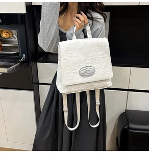Detail des weißen Rucksacks mit geprägter Blumentextur und silberner Metallplakette