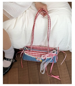 Close-up of denim baguette bag featuring red gingham straps and lace bow details