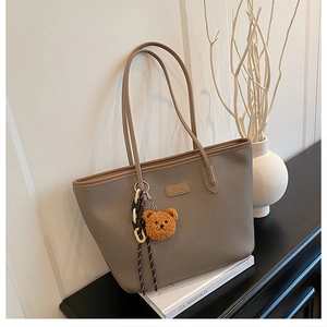 Dettaglio della borsa tote con texture litchi, ciondolo a orso e targhetta in pelle