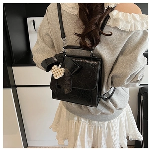 Detail of black glossy bow backpack with pearl heart charm and ruffled texture