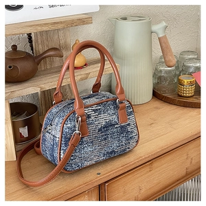 Detailed view of a blue sequin barrel bag with brown leather trim on a wooden table