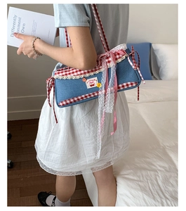 Detail of a denim underarm bag with lace trim, red gingham edges and a cherry patch