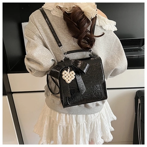 Detail of black glossy pleated crossbody bag with a decorative bow and pearl heart charm