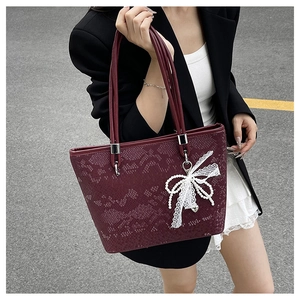 Close-up of burgundy lace tote bag with pearl bow charm and silver metallic hardware