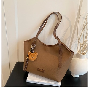Detail of caramel brown tote bag with pebble leather texture and cute bear charm accessory