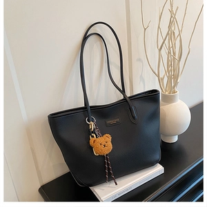 Dettaglio borsa tote in pelle nera a grana con logo in metallo e ciondolo a forma di orso