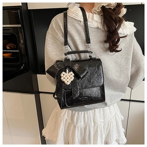 Detail of black glossy bow backpack with a white pearl heart pendant in a stylish setting