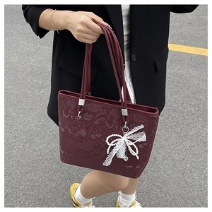 Detail of burgundy textured leather tote bag with lace bow and pearl charm accessory