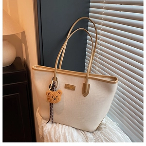 Dettaglio borsa tote beige a grana con placca moda e ciondolo a forma di orsetto