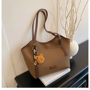 Close-up of brown pebbled leather tote bag featuring a cute plush bear charm decoration