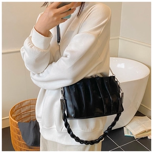 Detail shot of black pleated crossbody bag with woven handle and metal chain on a model