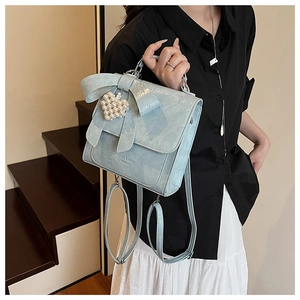 Detail of light blue bow backpack with pearl heart charm worn by model on stairs
