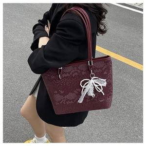 Close-up of burgundy snakeskin tote bag with pearl bow charm and silver hardware