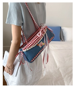 Detail of blue denim baguette bag with red gingham trim and cherry lace decoration