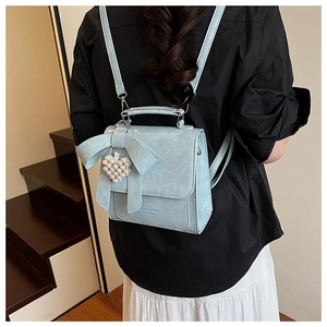 Detail of light blue bow backpack with heart pearl pendant shown on model
